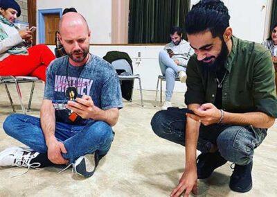 Two young men kneeling and reading theatre scripts at TELL Community Gathering in April of 2023