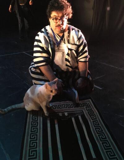 Majdi wearing black and white striped robes sitting down on floor with a stray cat