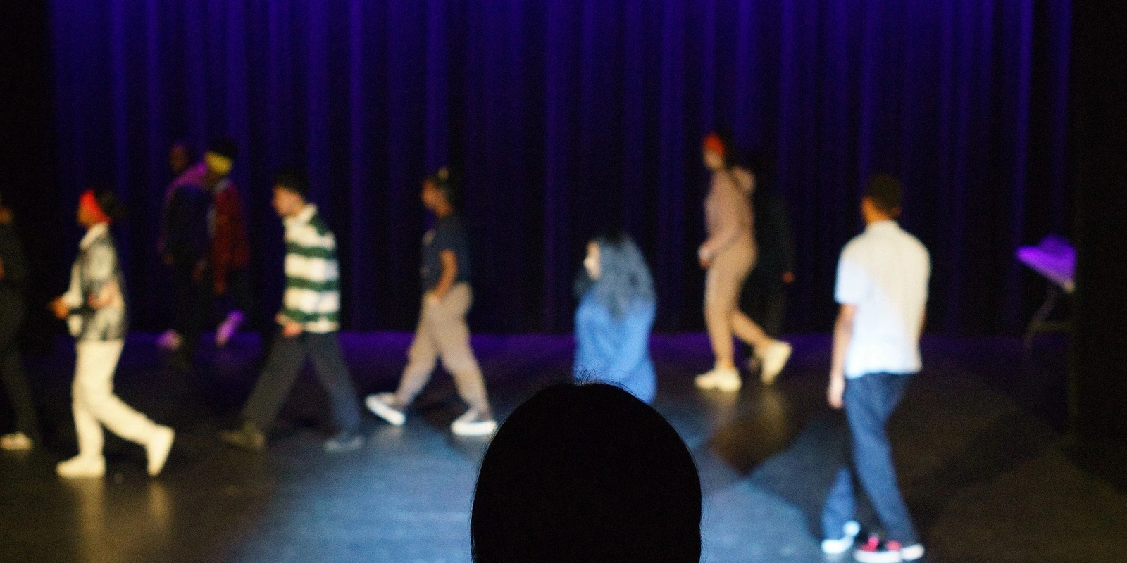 Newcomer Youth Theatre Program students walking on a stage during an exercise or performance.