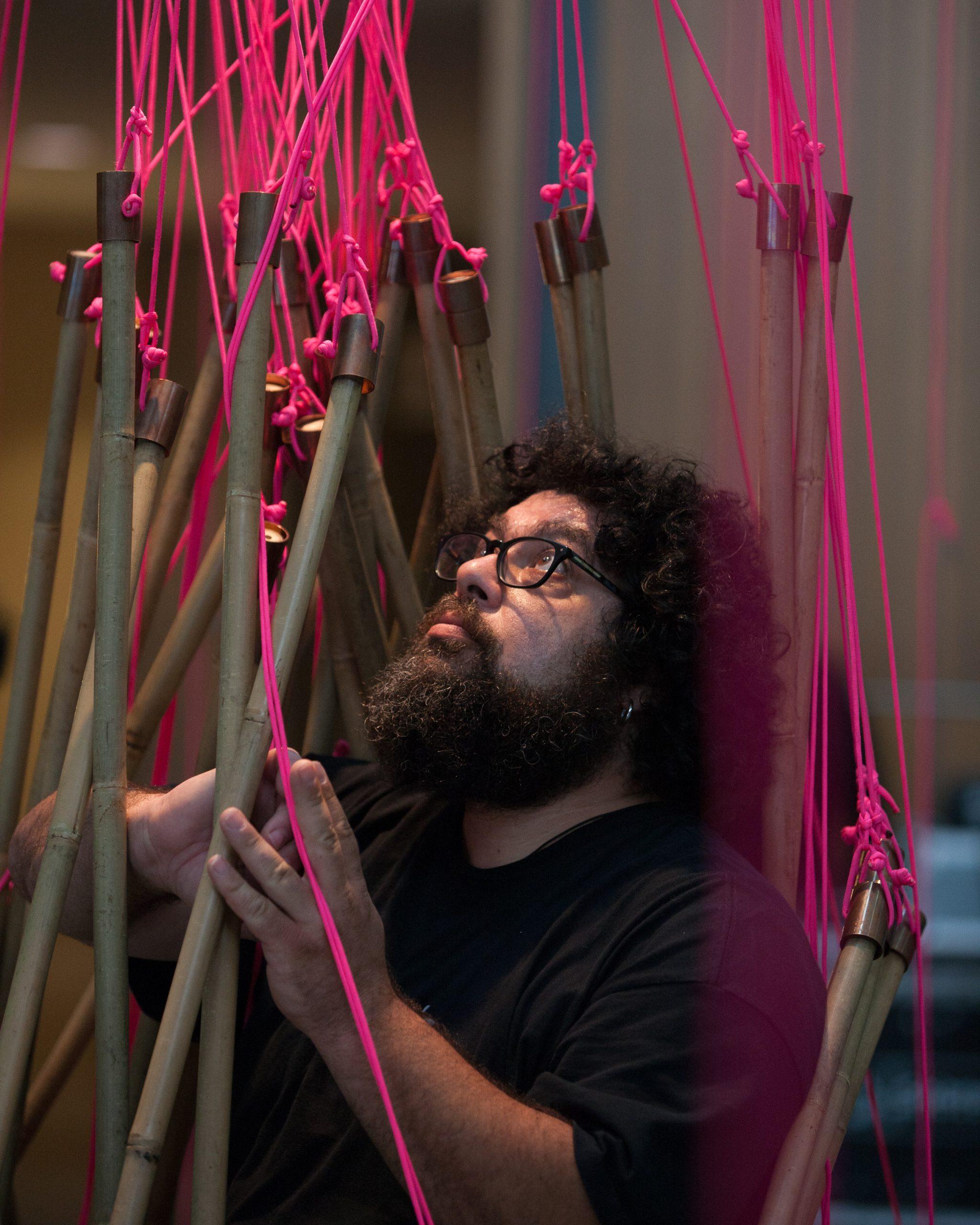  Majdi interacts with art installation, where he is surrounded by bamboo sticks that are tied up with pink string