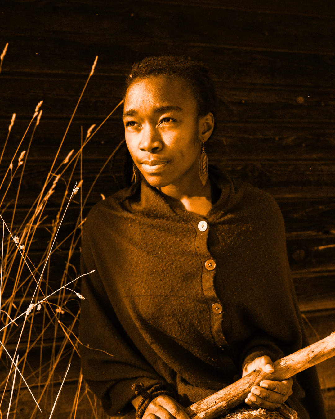 A woman wearing a cloak and carrying a walking stick next to some wheat