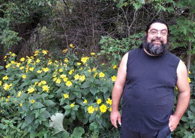 Majdi posing by yellow flowers while wearing a black tank top