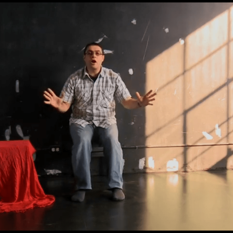 Man sitting on chair with arms out, while light pours in through the window and onto the wall behind him