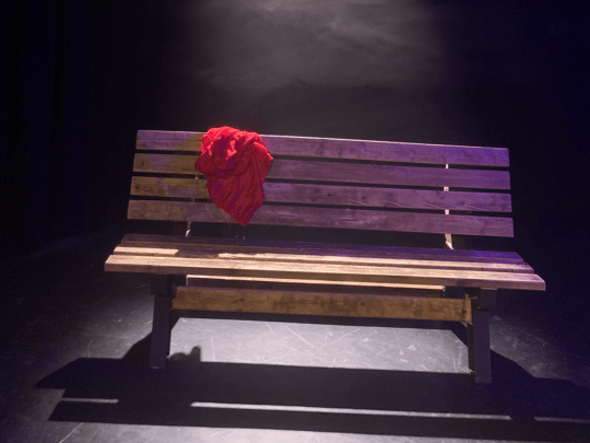 SOMETIMES IT SNOWS IN APRIL - 540x405 A Wooden bench with a red sweater sitting on a stage against a black background