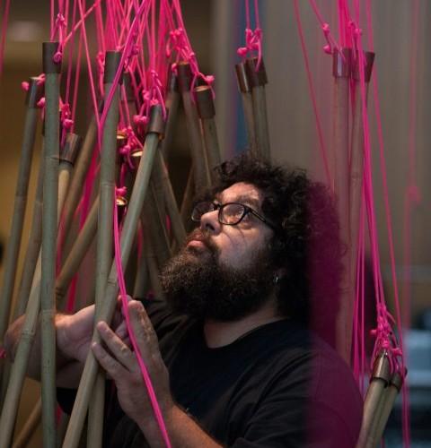 admin-ajax Majdi interacts with art installation, where he is surrounded by bamboo sticks that are tied up with pink string